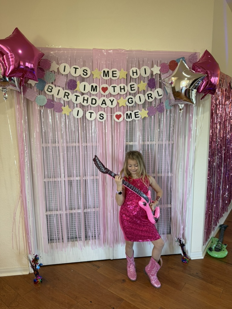 Birthday girl rocking out with an inflatable air guitar in front of the sparkly backdrop